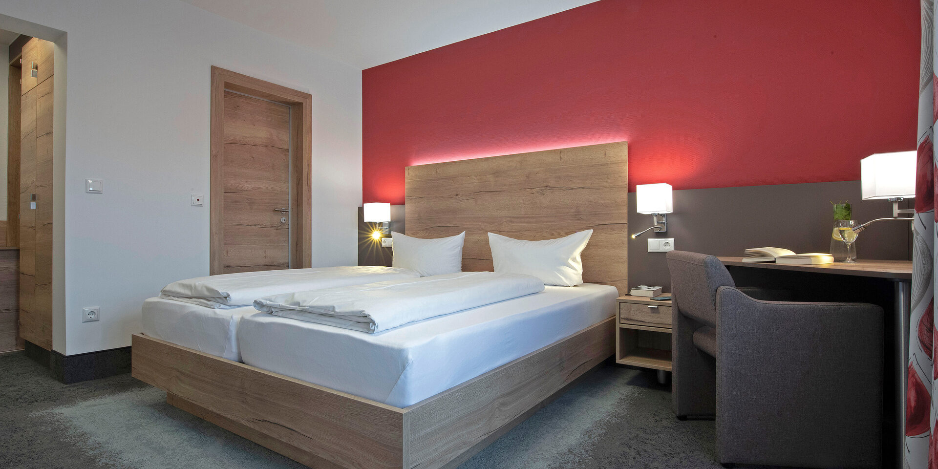 Der Schlafraum im Doppelzimmer Komfort Plus ist im rot weißen Stil gehalten.