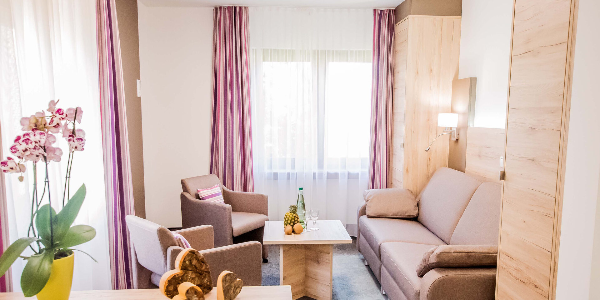 Der Wohnbereich eines Doppelzimmer Komfort Plus im Haus Manuela mit der Couch und einer Orchidee auf einem Regal.